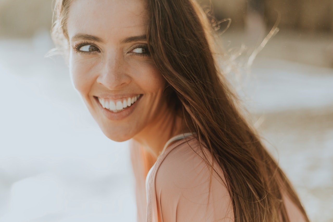 A beautiful middle-aged lady. Long haired. Smiling. Upper teeth fully visible. Someone who has had zirconium supported porcelain treatment before.