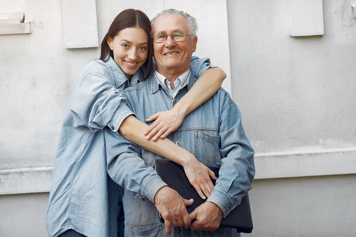 A young man is smiling next to his grandfather, hugging him. his teeth are showing