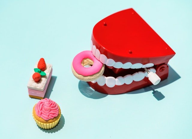 An iconic photographic narrative. There are some foods and a mouth miniature in the photo. If you overeat these sweets and do not take care of your teeth, your oral health will deteriorate.