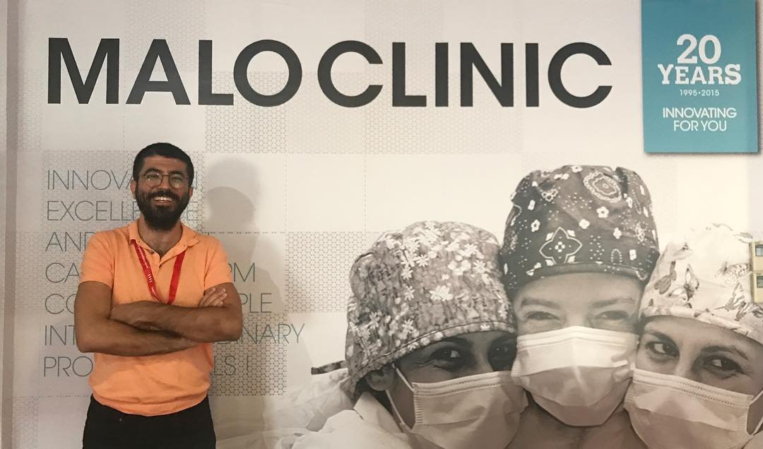 Doktor Çağdaş Çağlar Laçin bir standın önünde. Neşeli. Gözleri kapalı. Gülümsüyor. Dişleri görünüyor. Beyaz ve sağlamlar.