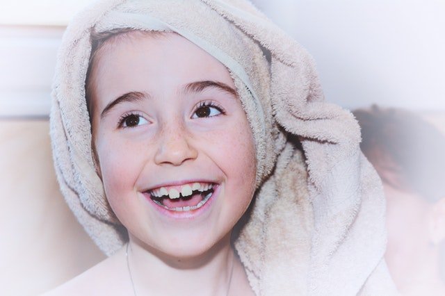 A 7-year-old girl wrapped in towels after a bath. She is smiling despite her missing teeth.